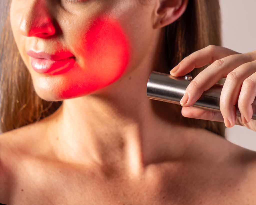 Woman Holding Bullet Red Light Therapy Device Towards Face